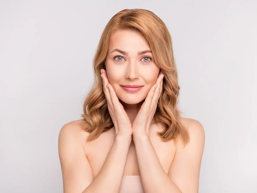 Middle-aged woman touching her smoother, shining face and smiling after receiving skin treatments.