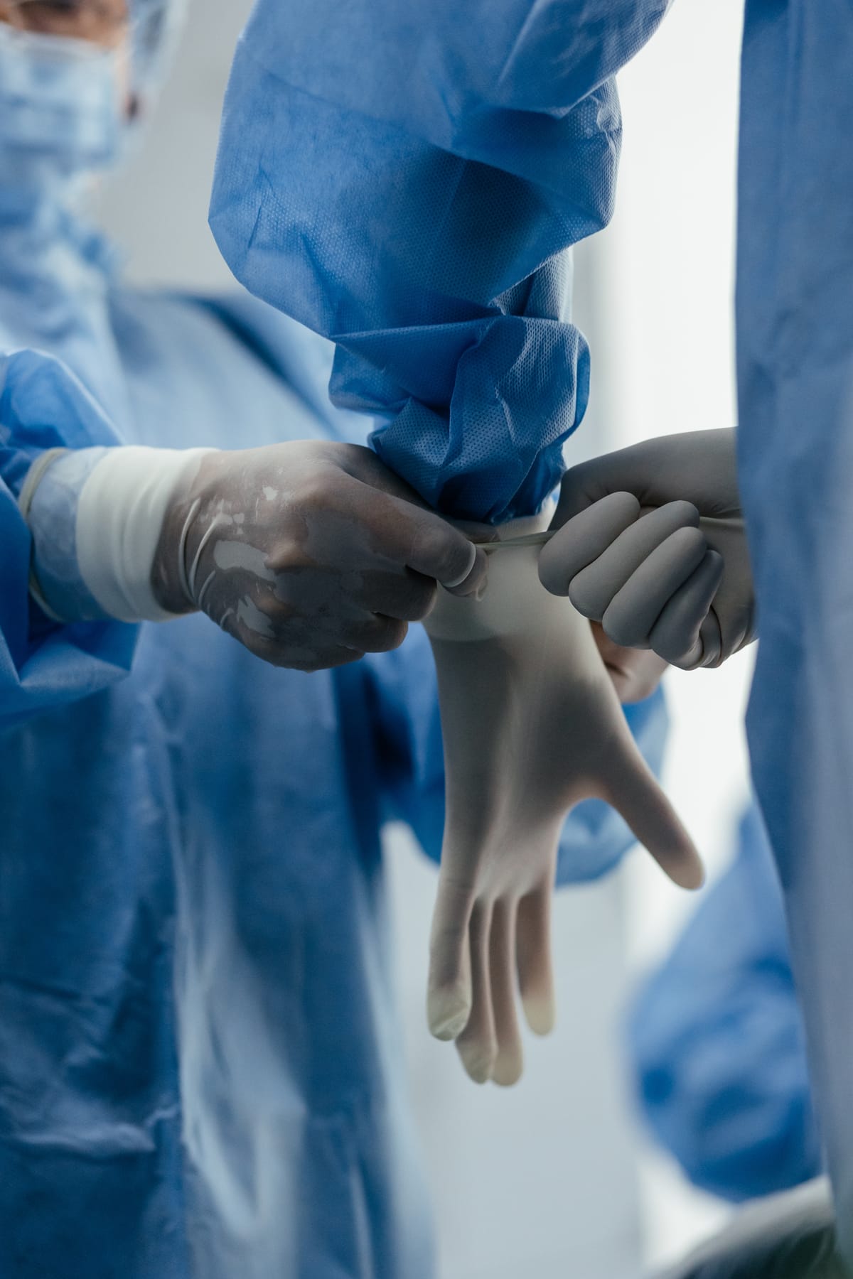 A surgeon in blue scrubs being helped into sterile gloves before a procedure (models)