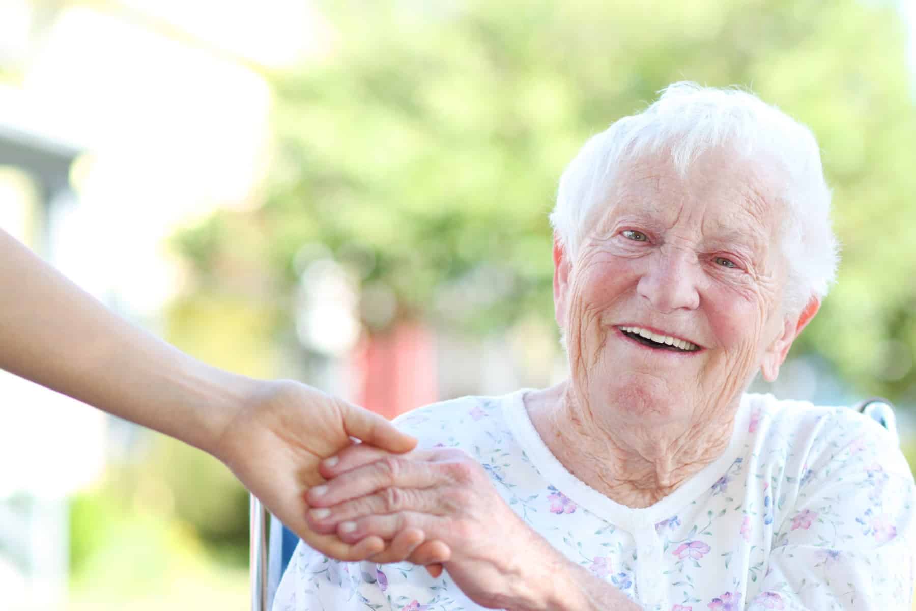 A smiling older woman holding a caregiver's hand outdoors (model)